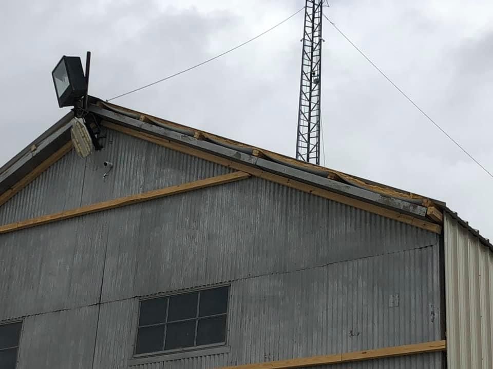 A corrugated metal building with a visible roofline, outdoor lighting fixtures, and a tall antenna tower behind it.