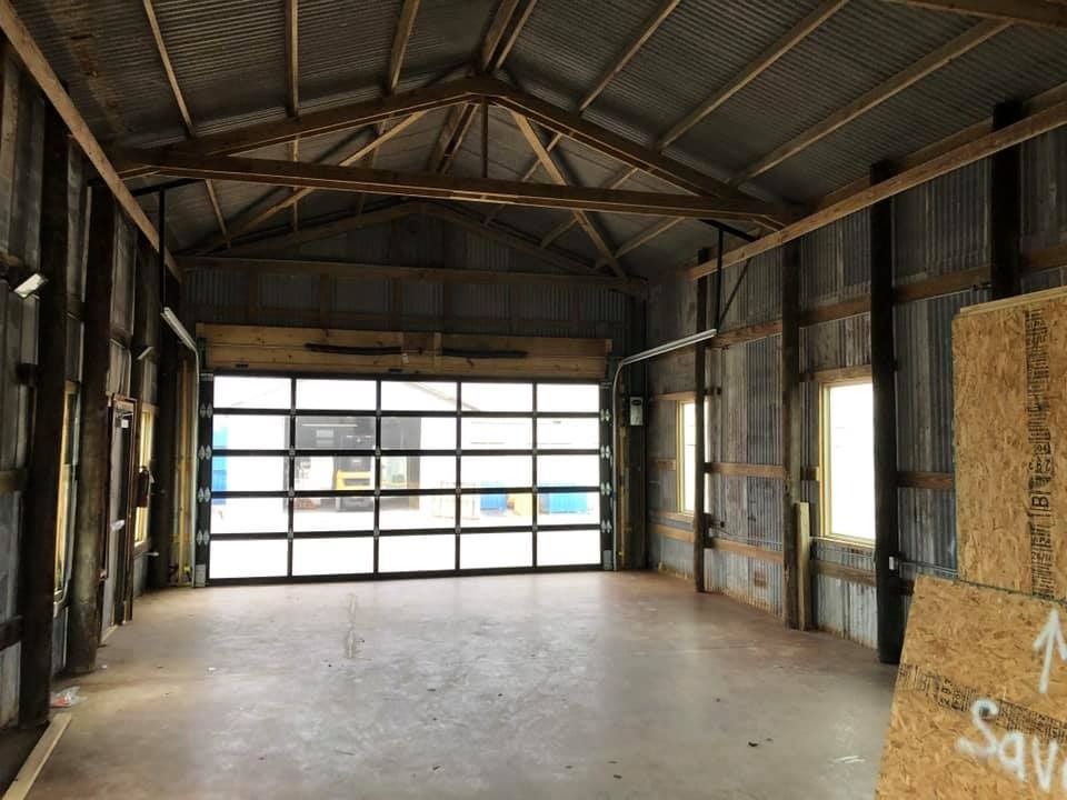 Empty, spacious rustic garage with exposed wooden beams, corrugated metal walls, concrete floors, and a glass-paneled door.