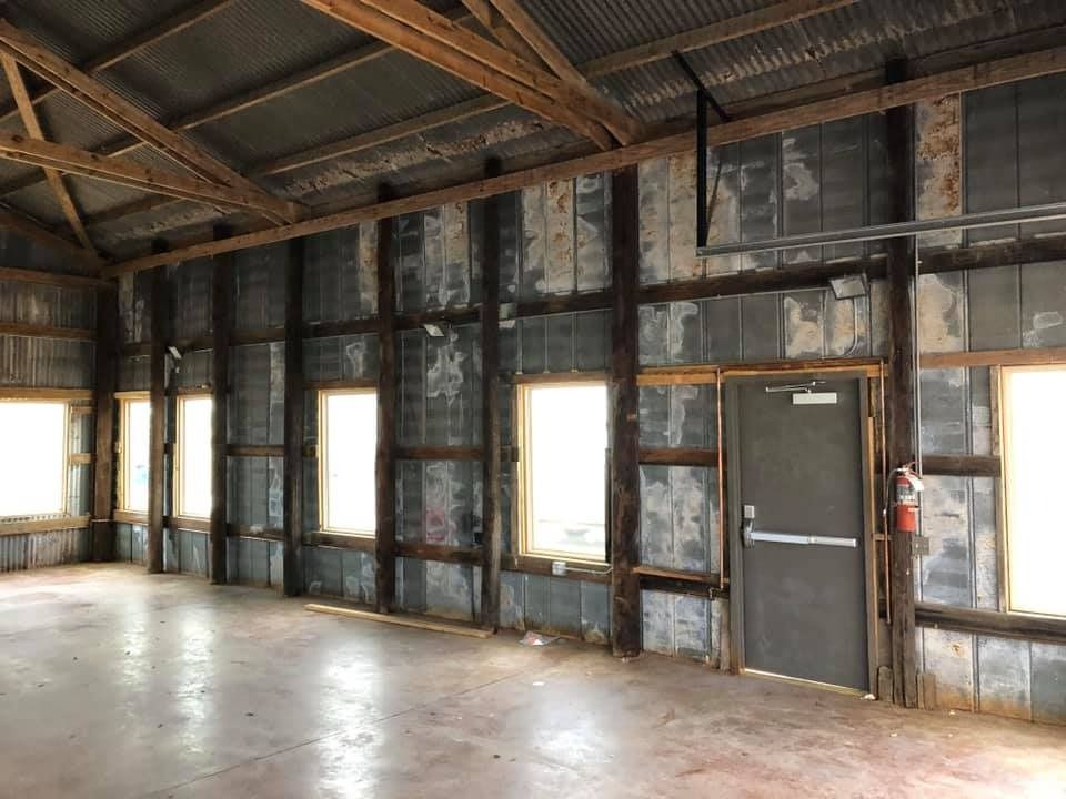 Interior of a rustic building with a concrete floor, corrugated metal walls, wooden beams, and a closed metal exit door.