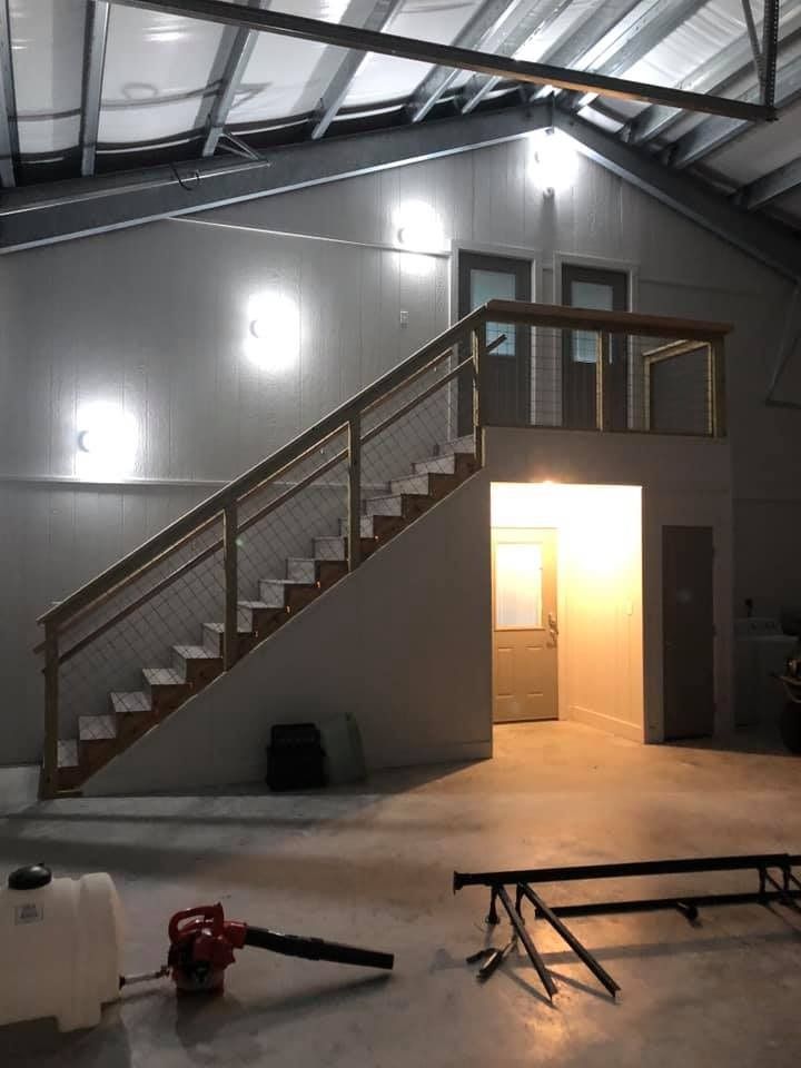 An indoor workspace featuring a wooden staircase with metal railings leading to a mezzanine, plus doors and bright lights.