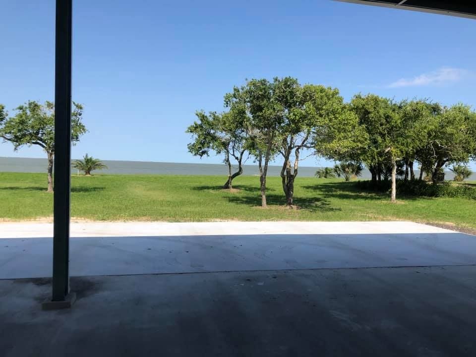 A view from a shaded patio looking out over a grassy field toward the ocean under a clear blue sky.