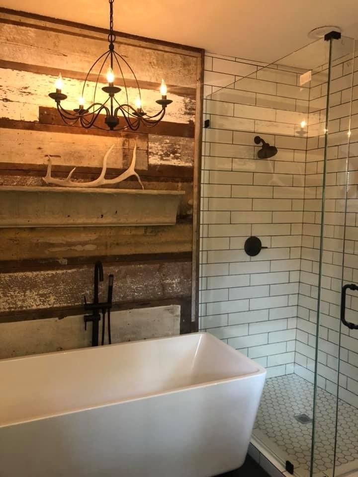 Modern bathroom featuring a white soaking tub, rustic reclaimed wood wall with antler decor, and a glass-enclosed shower.
