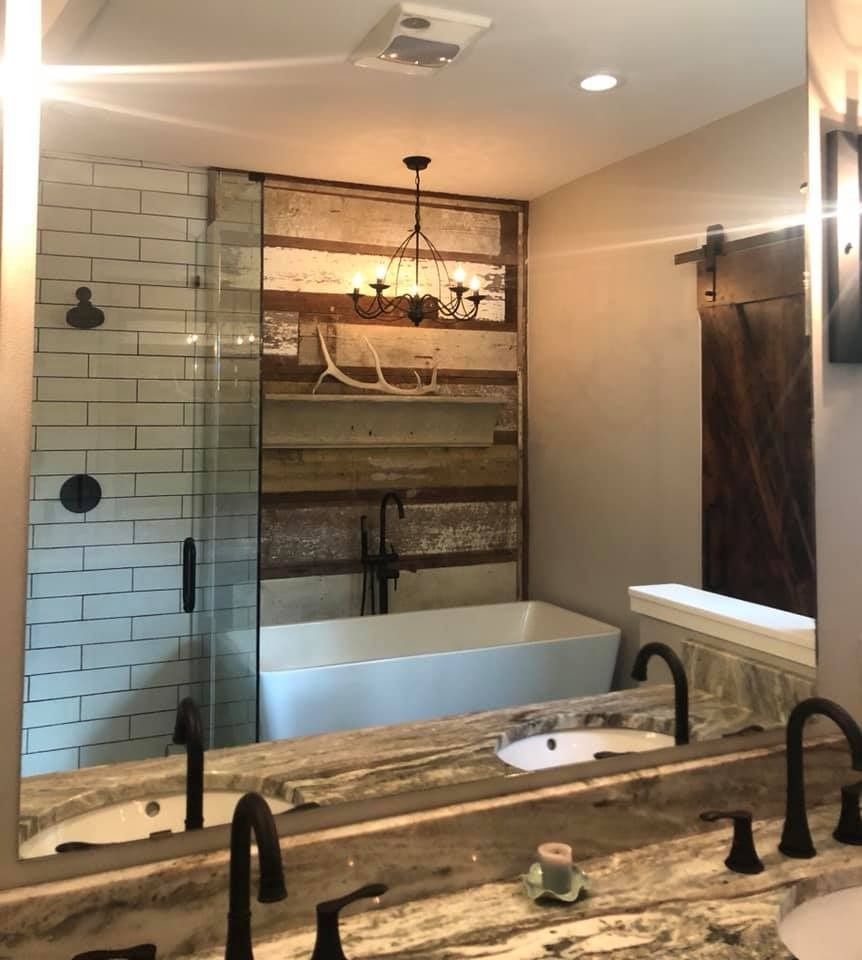 A bathroom view featuring a freestanding white tub, a glass-enclosed shower, reclaimed wood wall, and granite countertops.