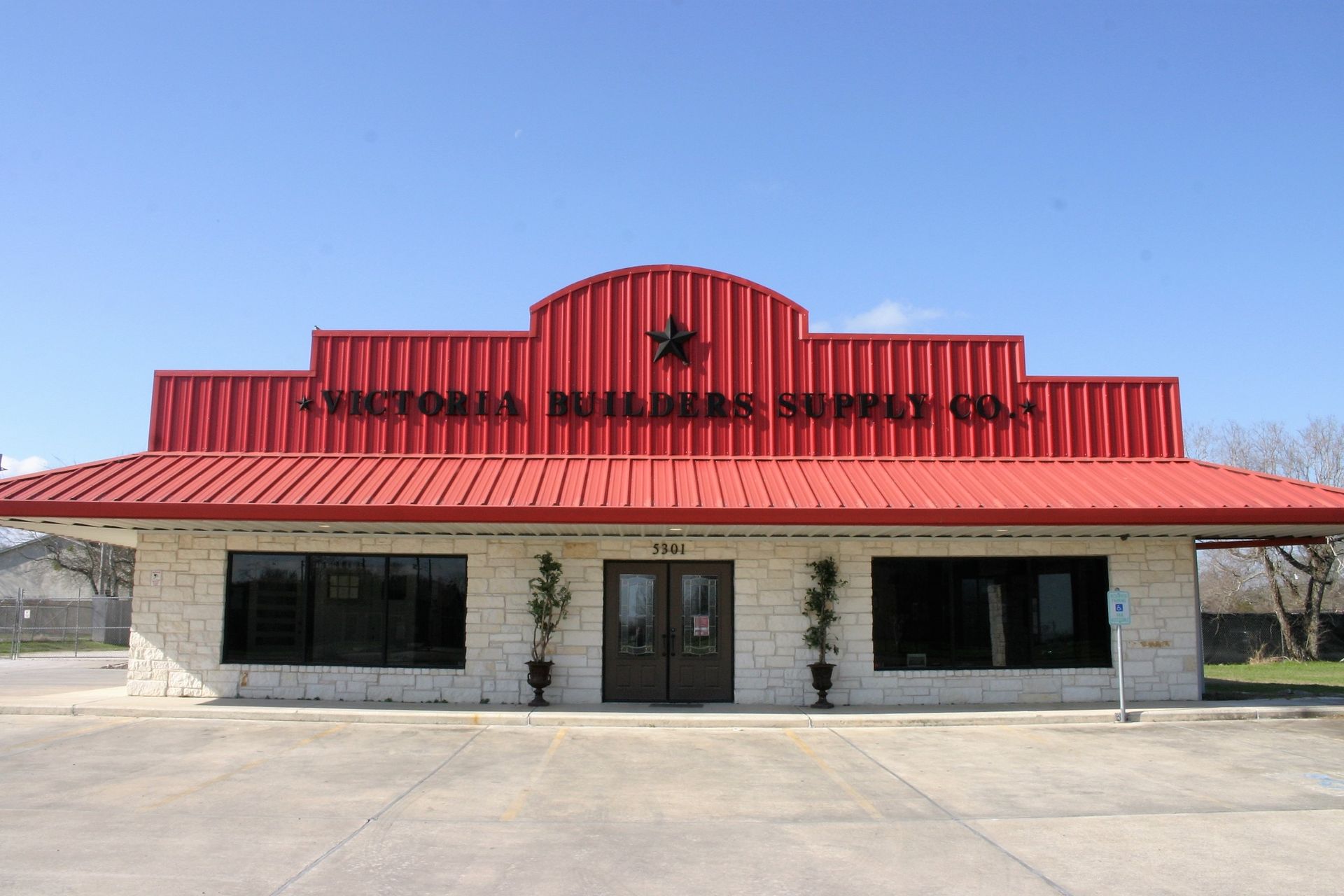 Victoria Builders Supply Co. storefront with a red metal roof, stone walls, and a large star emblem.