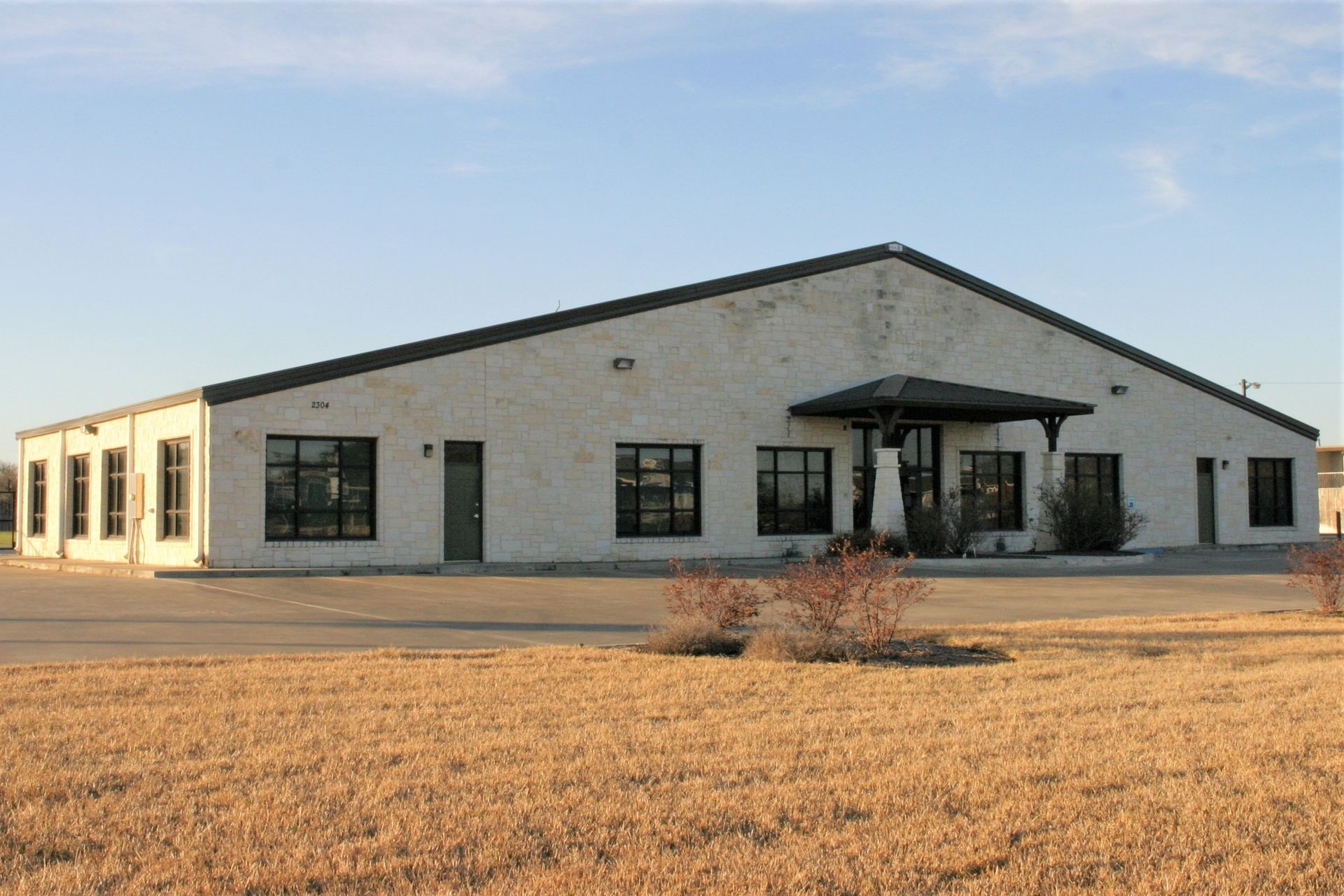 A single-story, light-colored stone commercial building with dark window frames and a central covered entrance.