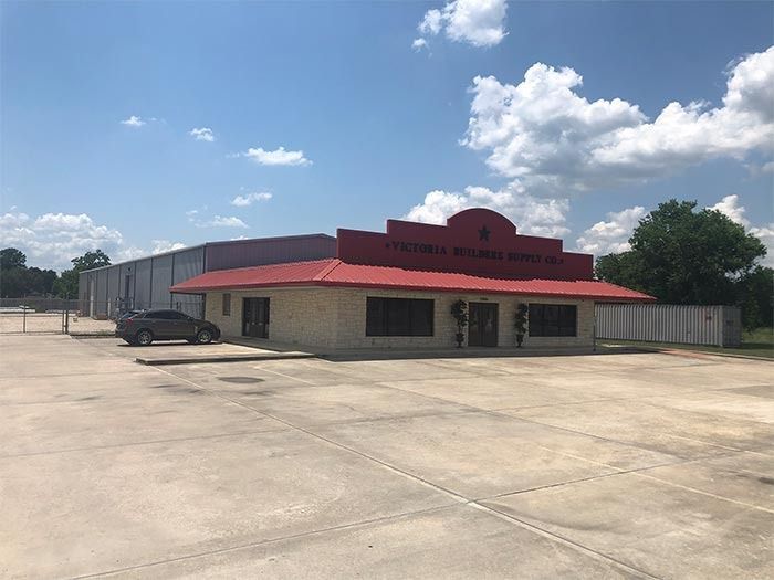 A single-story commercial building with a red roof and light-colored stone facade under a sunny blue sky.