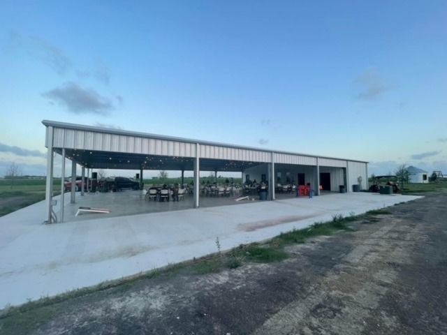 An outdoor metal event pavilion with open sides, tables, and seating on a concrete patio at sunset.