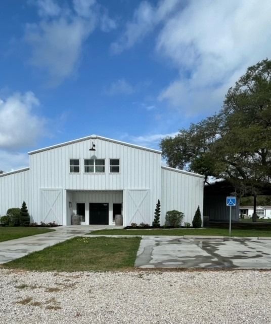 A white metal building under a blue sky, featuring a central entrance, gravel foreground, and a handicapped parking sign.