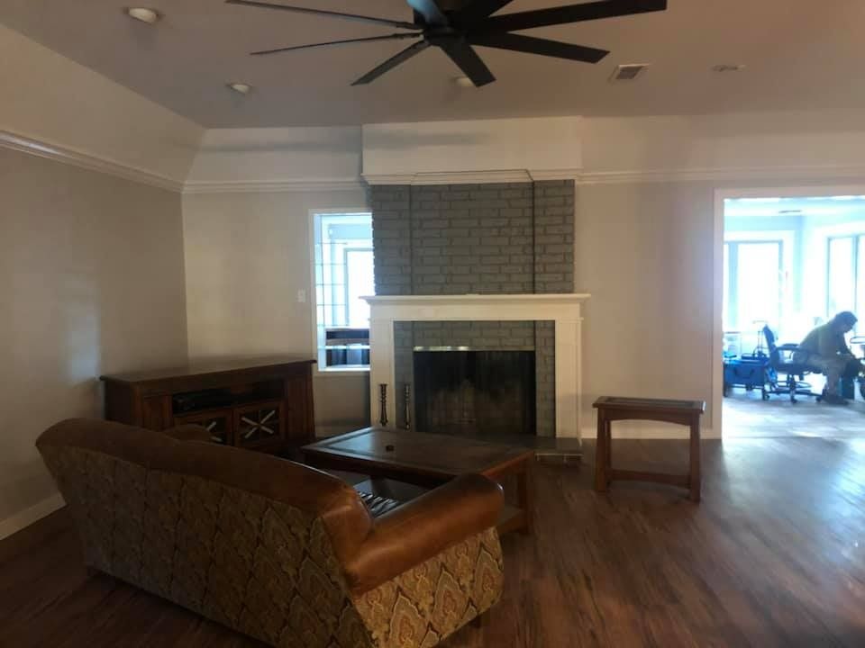 A living room featuring a brown sofa, a dark wood coffee table, and a grey brick fireplace under a ceiling fan.