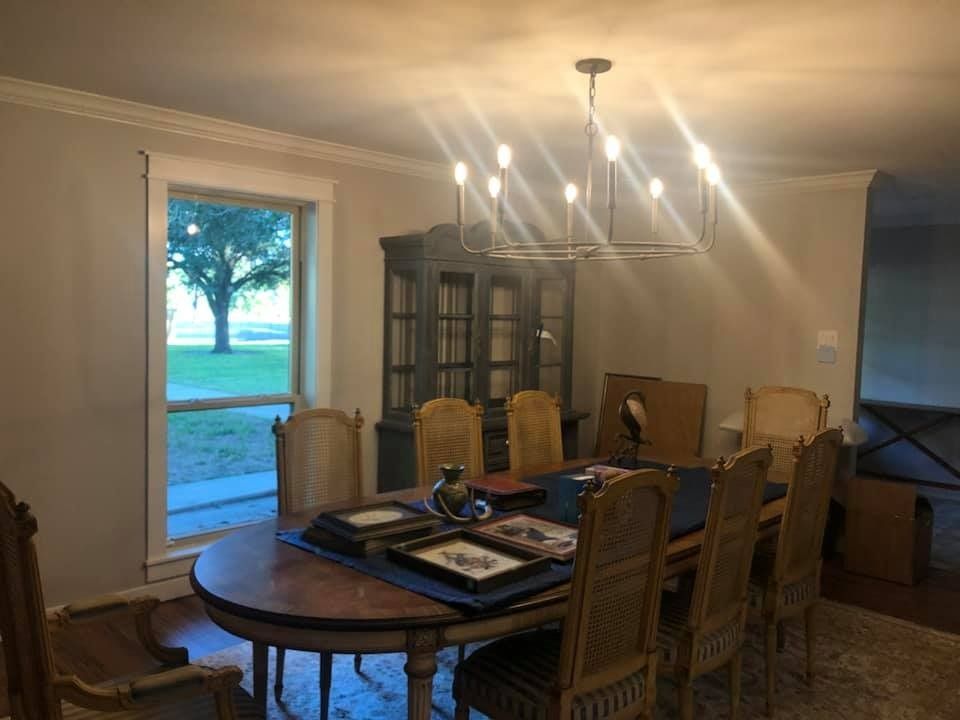 A dining room with an oval wooden table, six chairs, a large hutch, and a chandelier, situated by a window with a view.