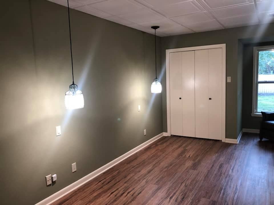 A room with olive green walls, wood-look flooring, two hanging pendant lights, a white closet, and a window.