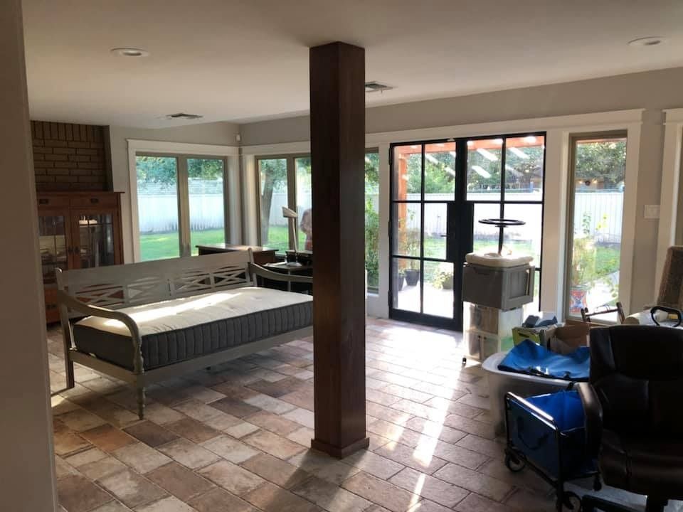 Sunroom with stone tile floor, a central wooden support pillar, a daybed, double glass doors, and scattered furniture.