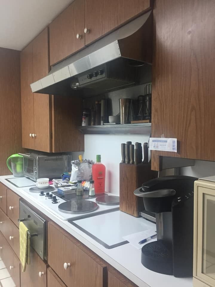 A kitchen counter with a stovetop, coffee maker, knife block, and wooden cabinets above a range hood.