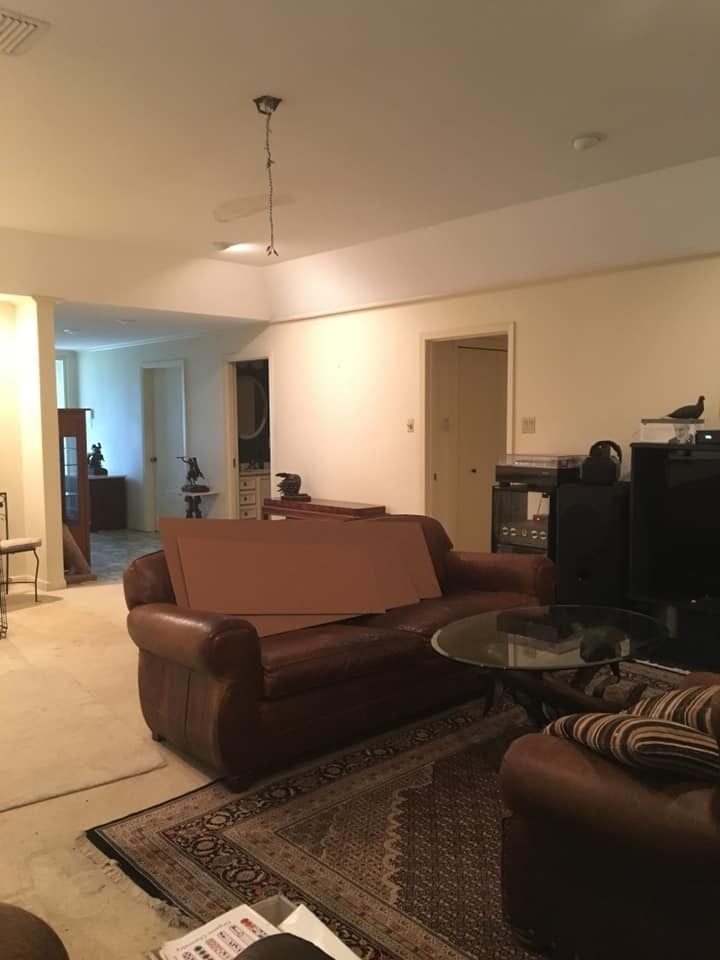 A living room with brown leather furniture, a patterned area rug, a glass coffee table, and an open doorway.