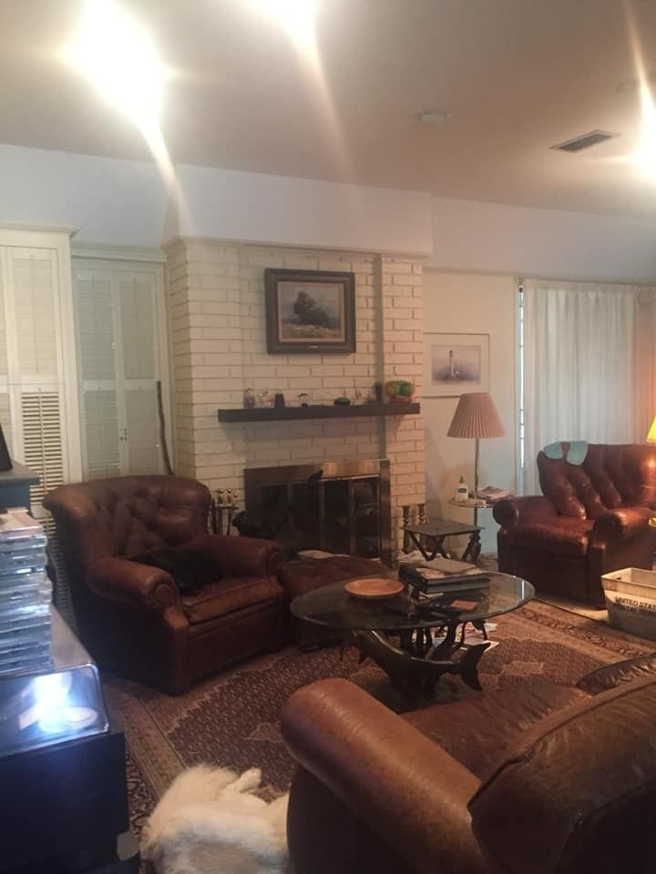 A living room with leather chairs, a white brick fireplace, a glass coffee table, and an ornate area rug.