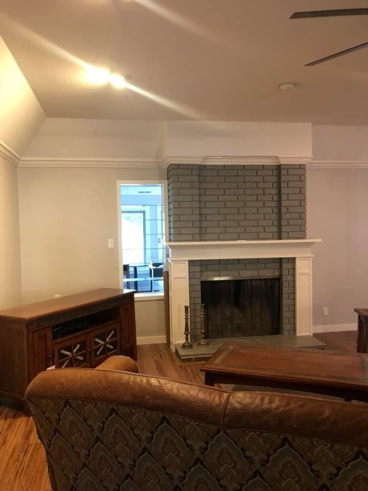 A gray brick fireplace with a white mantel sits beside a wooden media console in a living room with light walls.