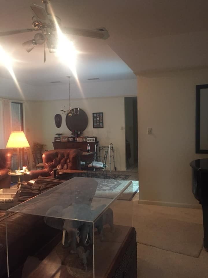 A living room featuring leather furniture, a glass coffee table, a ceiling fan, and a piano in the foreground.