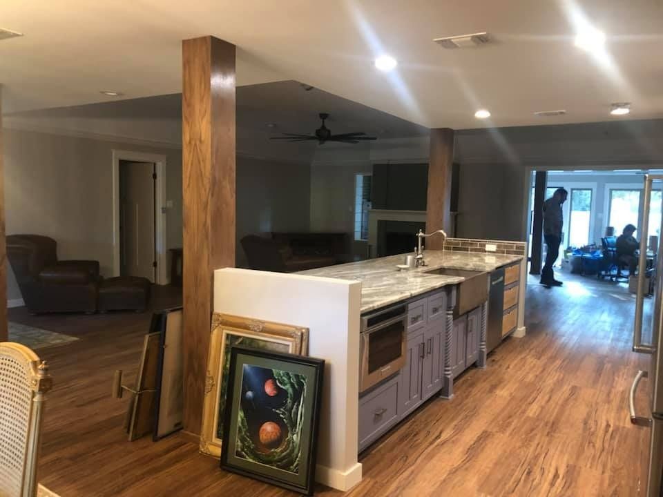 A spacious, open-concept kitchen and living area featuring wood floors, a large island, and wood support columns.