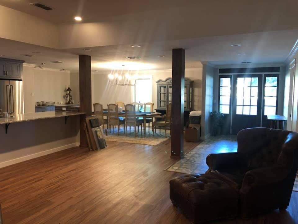 An open-concept living area with a brown leather armchair, wooden support pillars, a dining set, and a kitchen counter.