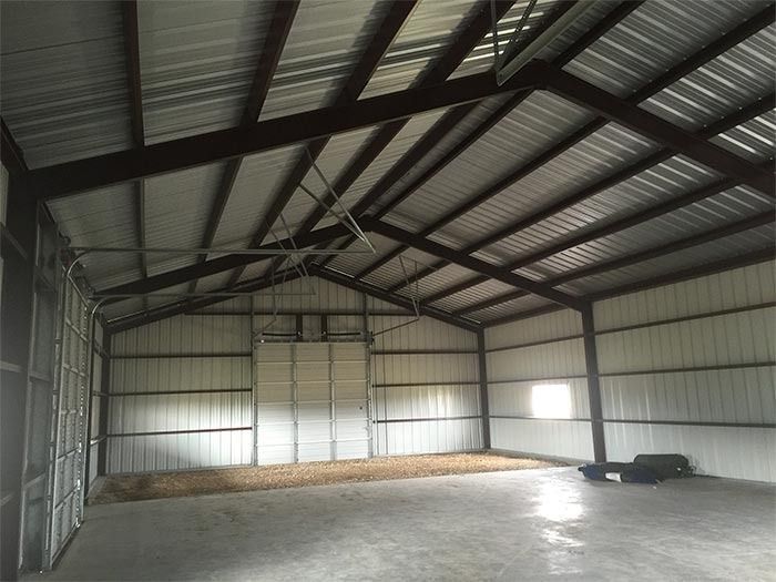 An interior view of a spacious, empty metal building with concrete floors, steel framing, and a white metal wall finish.