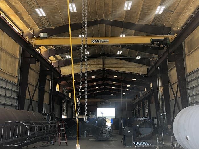 Interior of a metal workshop with an overhead bridge crane, high ceiling, and various industrial equipment.