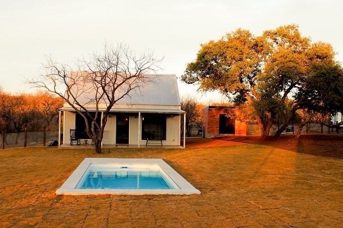 A small white cottage with a pool in the front yard, framed by trees under a golden sunset sky.