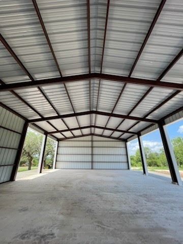 An interior view of a wide, open metal building with a concrete floor, a gabled roof, and steel support beams.