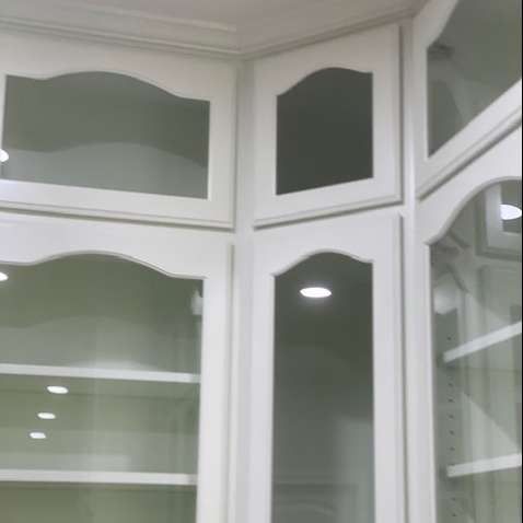White kitchen cabinets with glass doors, shelves, and integrated lighting in an L-shaped corner configuration.