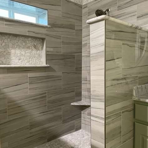 A modern walk-in shower with horizontal gray-veined tiles, a mosaic-tiled recessed shelf, and a built-in corner seat.