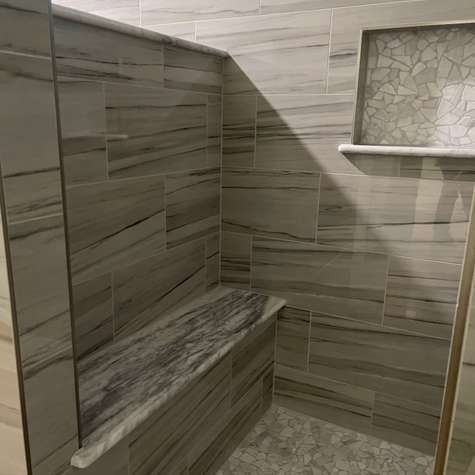 A tiled shower corner featuring a built-in stone bench, gray horizontal stone-look wall tiles, and a mosaic tiled niche.