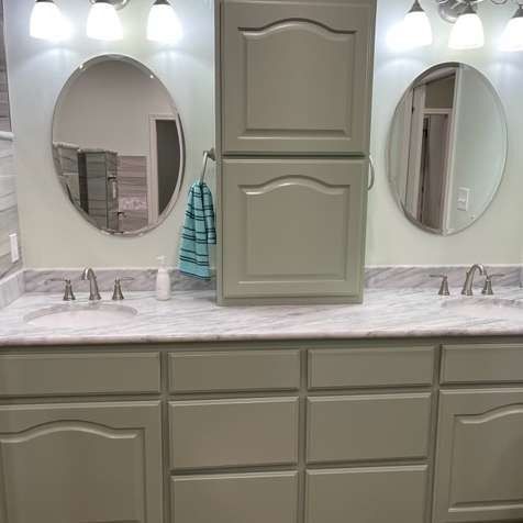 A bathroom double vanity with light gray cabinets, a marble countertop, two oval mirrors, and a central storage tower.