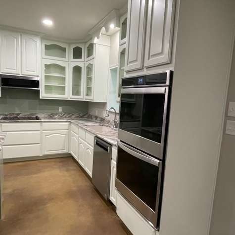 A kitchen with white cabinets, dark countertops, concrete-style flooring, and a stainless steel wall oven.