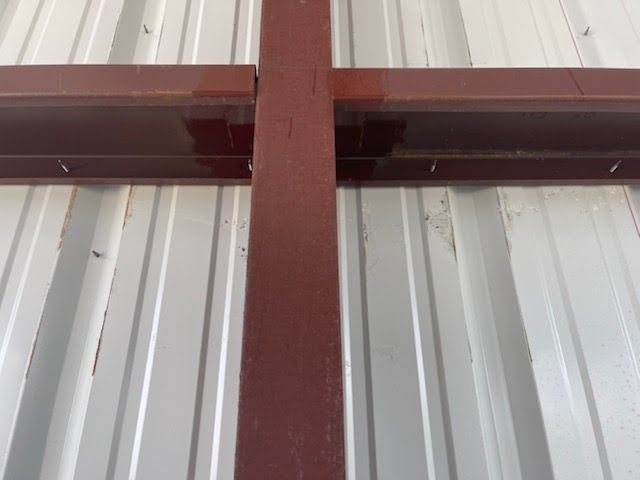 A brown metal cross-beam assembly mounted against a white corrugated metal wall.
