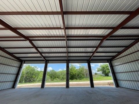Interior view of an open-sided steel carport with a concrete floor, metal roof, and a scenic outdoor landscape.