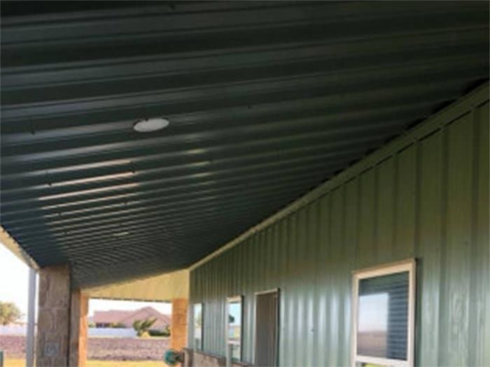 An angled view of a house exterior featuring dark green vertical metal siding, a covered porch, and stone-wrapped pillars.