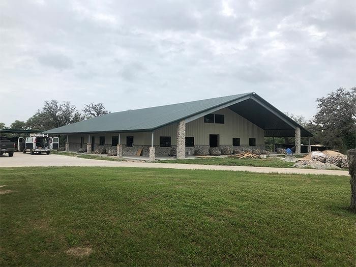 A large, single-story building with a green gable roof, stone pillars, and a wide covered porch, set on a grassy lawn.