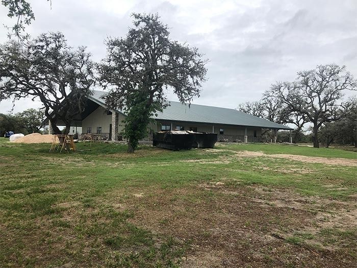 A wide, low-slung building with a large green roof stands in a grassy field dotted with trees under a cloudy sky.