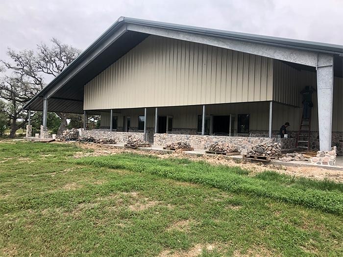 A partially constructed metal-sided building with stone masonry along the base, surrounded by a grassy landscape.