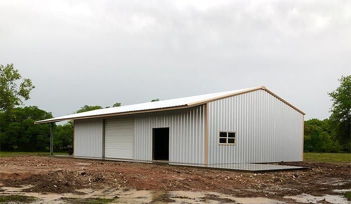 A newly constructed metal building with a white roof and silver corrugated walls, set in a rural, muddy field.