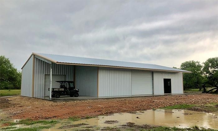 A metal shed with a side-open carport area, a roll-up door, and a single door on a dirt lot under a cloudy sky.