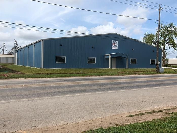 A blue, single-story metal commercial building with a central entrance and windows, seen from a roadside.