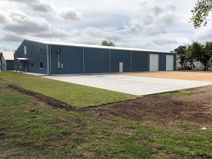 A blue, single-story metal warehouse building with white trim, located on a lot with a concrete pad and grass.