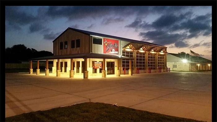 A modern fire station at dusk, illuminated with warm lighting, featuring large glass garage doors and a metal exterior.