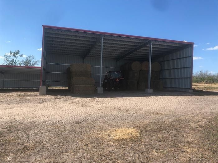 A metal open-sided shed with hay bales stacked inside and an all-terrain vehicle parked in the center.