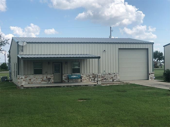 A metal-sided workshop with a front porch, stone base, and roll-up garage door under a cloudy sky.