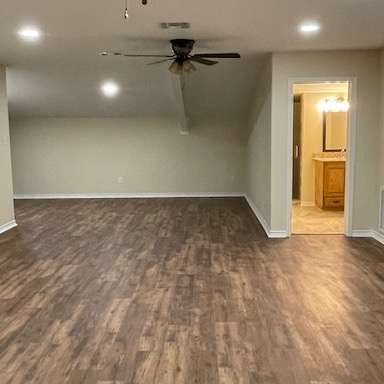 An empty room with wood-look flooring, a ceiling fan, recessed lighting, and a doorway leading into a beige bathroom.