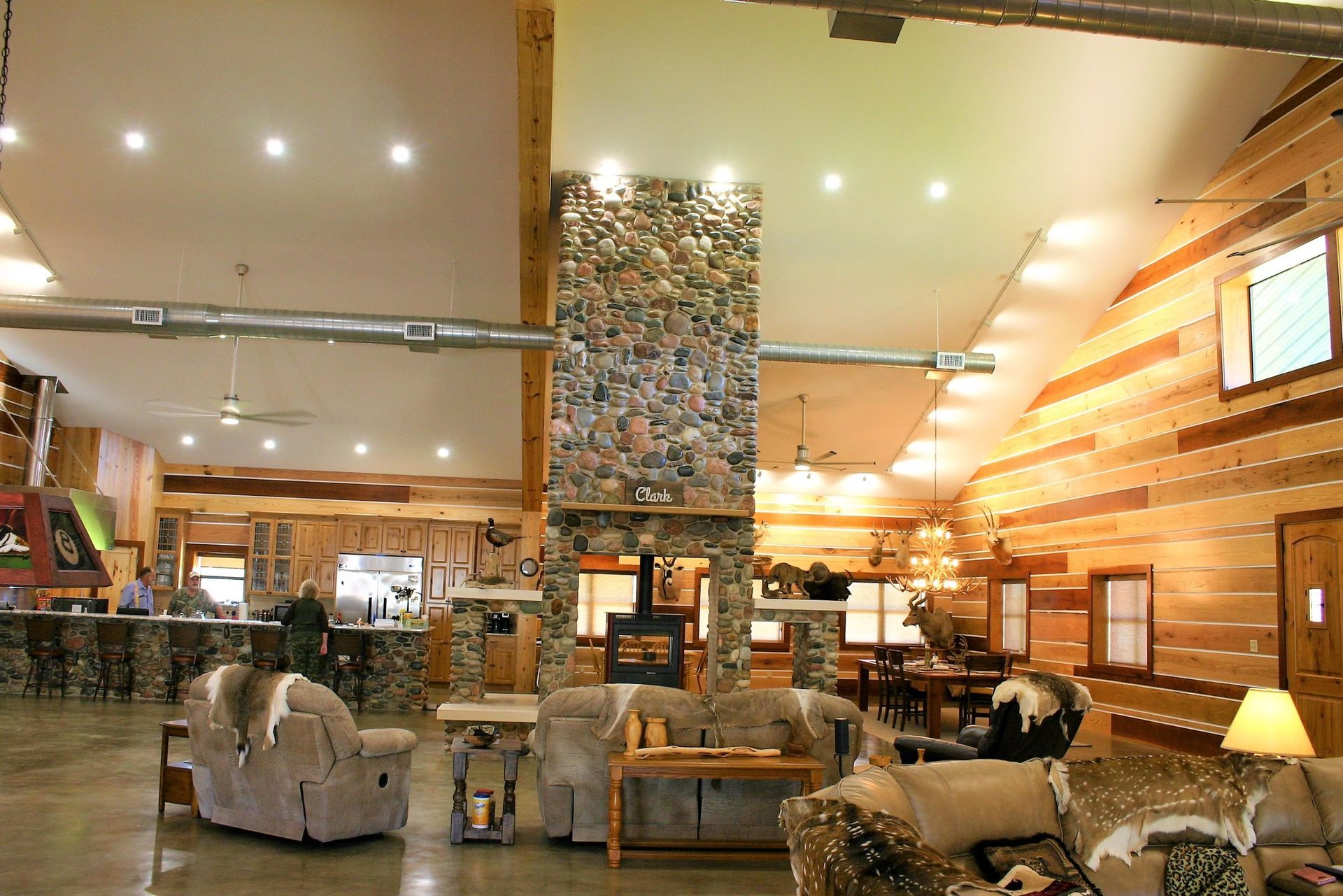 Spacious rustic lodge interior featuring a central stone fireplace, vaulted wood ceiling, and comfortable seating areas.