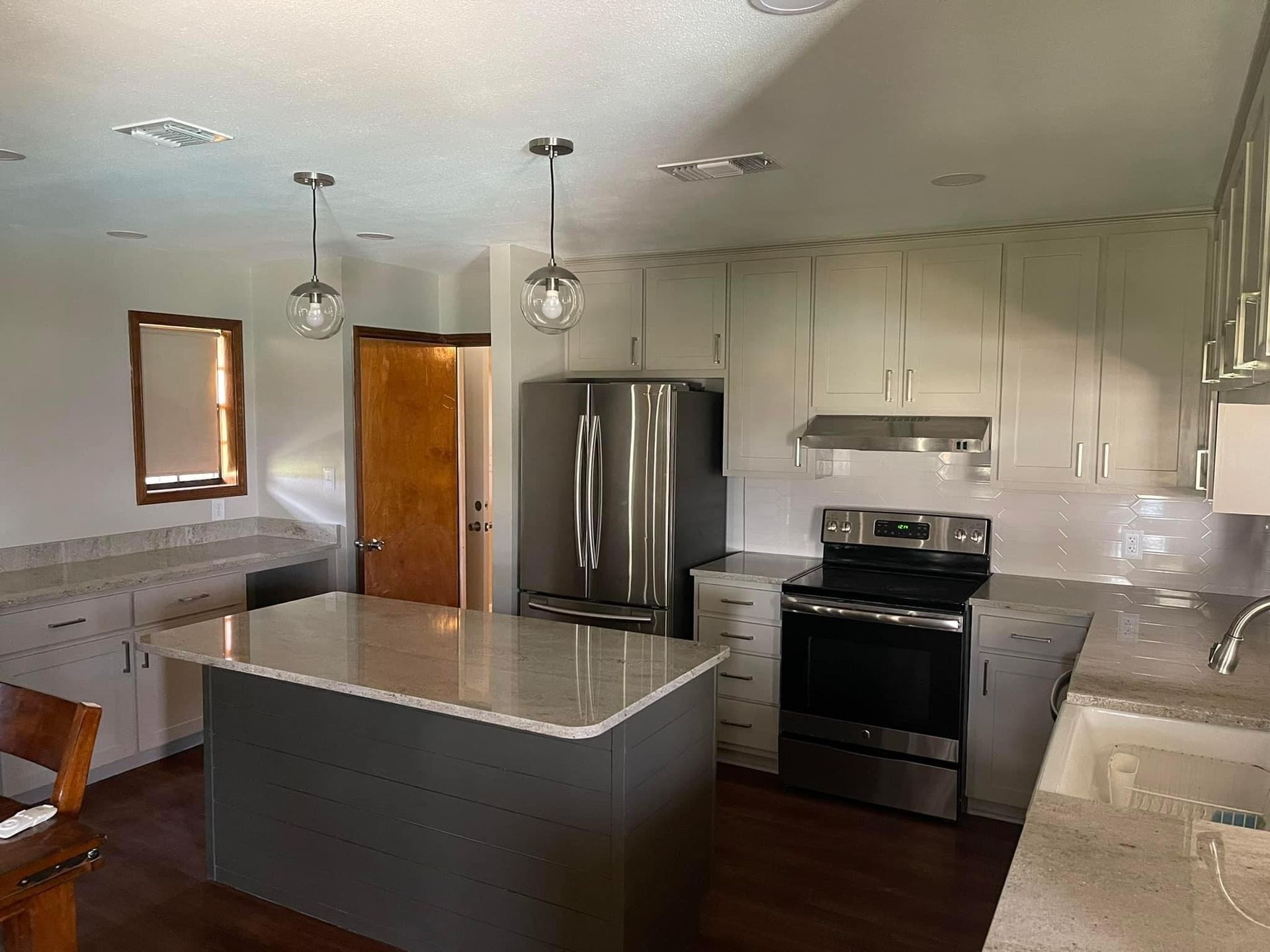 A kitchen with a dark grey island, white cabinets, stainless steel appliances, and a wood door.