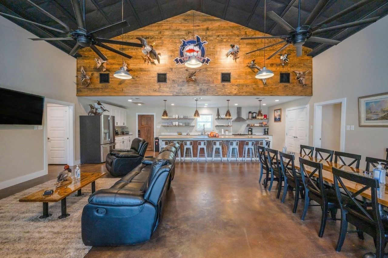A rustic living area with leather recliners, a wooden coffee table, a kitchen bar, and a vaulted ceiling with mounted decor.