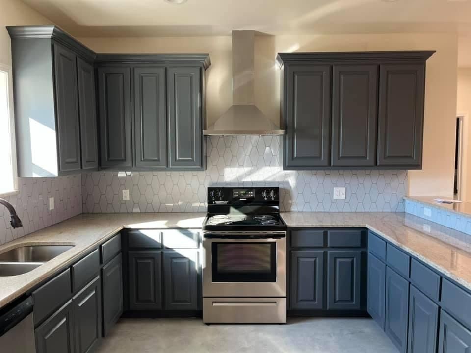 A kitchen with dark gray cabinets, stainless steel appliances, a range hood, and light-colored countertops.